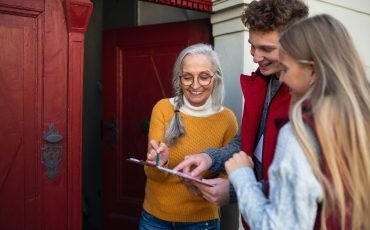 Young door to door volunteers talking to senior woman and taking survey at her front door